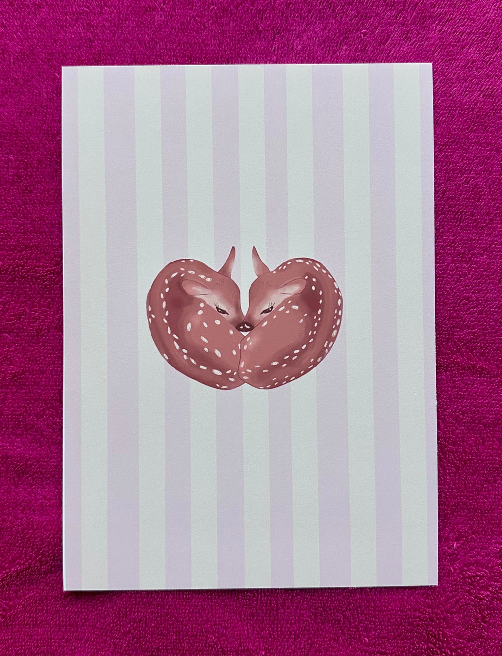 Note card with a fawn illustration on a striped background, placed on a purple surface
