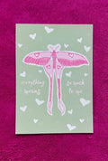 Card with pink butterfly illustration and text on a green background, placed on a purple textured surface.