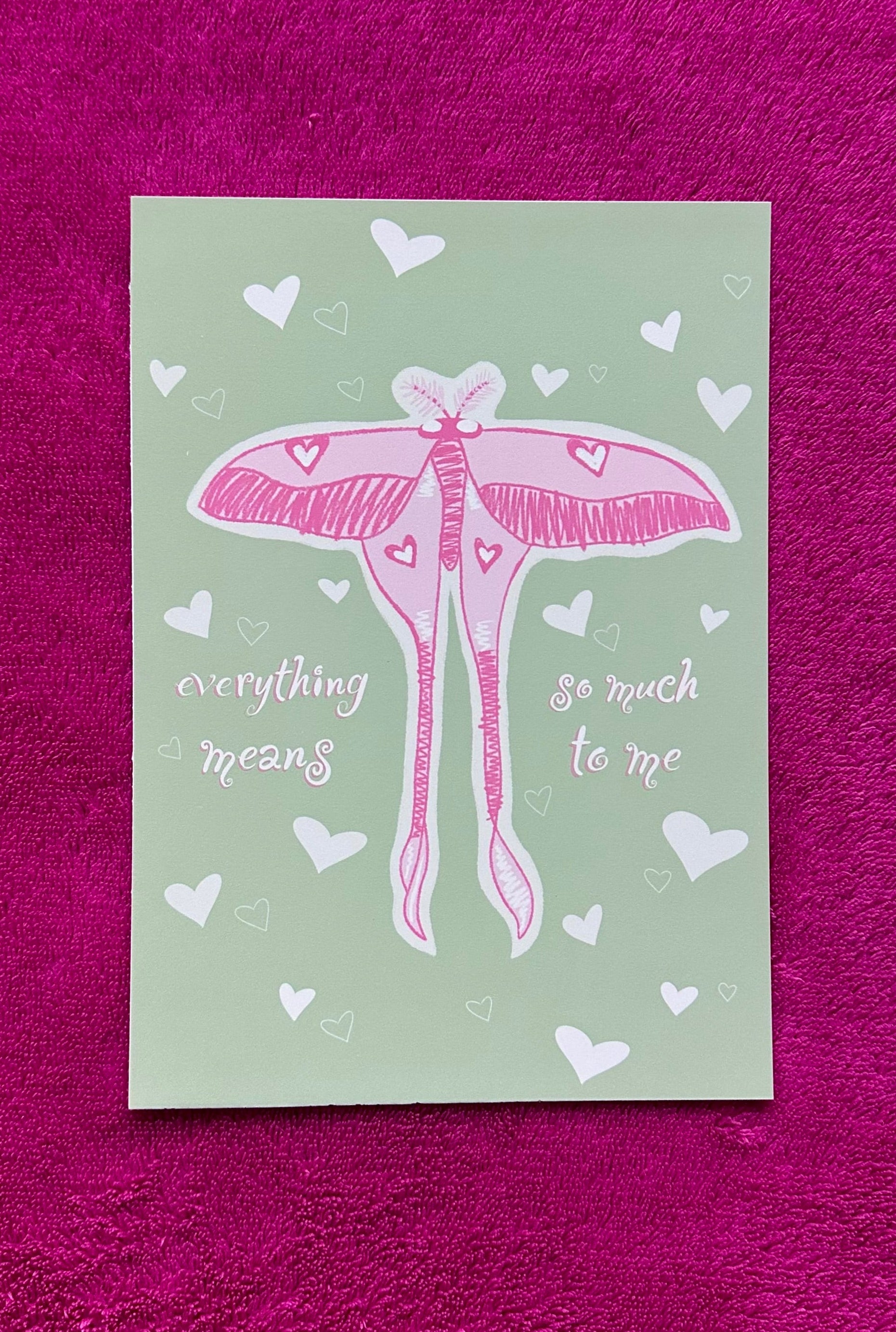 Card with pink butterfly illustration and text on a green background, placed on a purple textured surface.